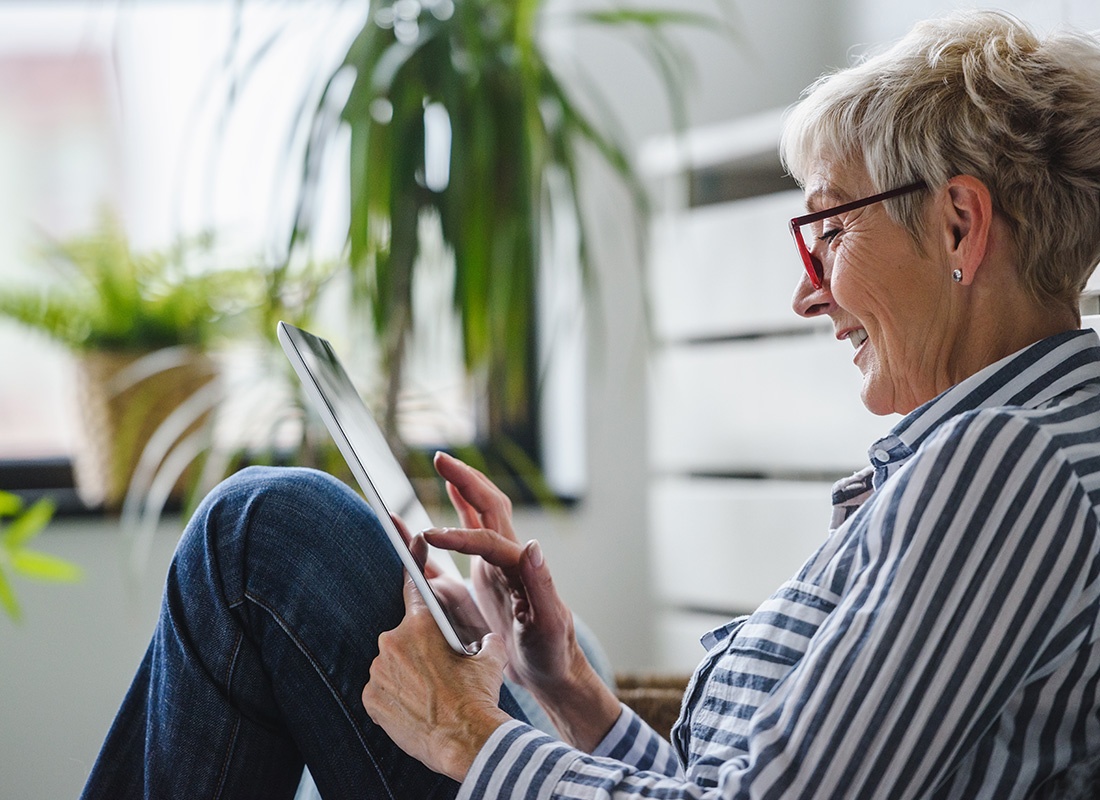 Online Portal - Older Woman Sitting Down by Her Plant Using Her Tablet